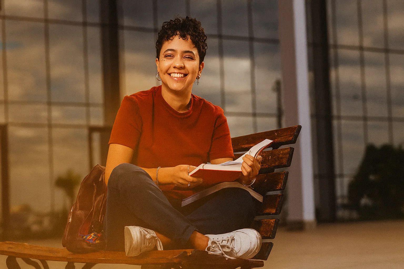 Estudante universitária sorridente sentada em um banco lendo um livro