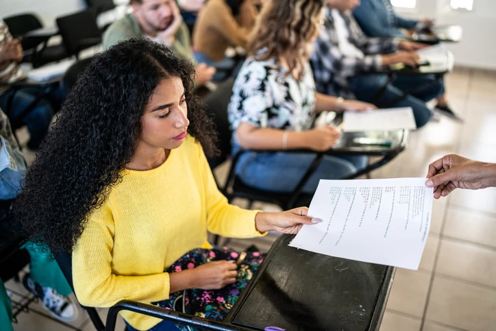 Estudante recebendo prova impressa em sala de aula universitária
