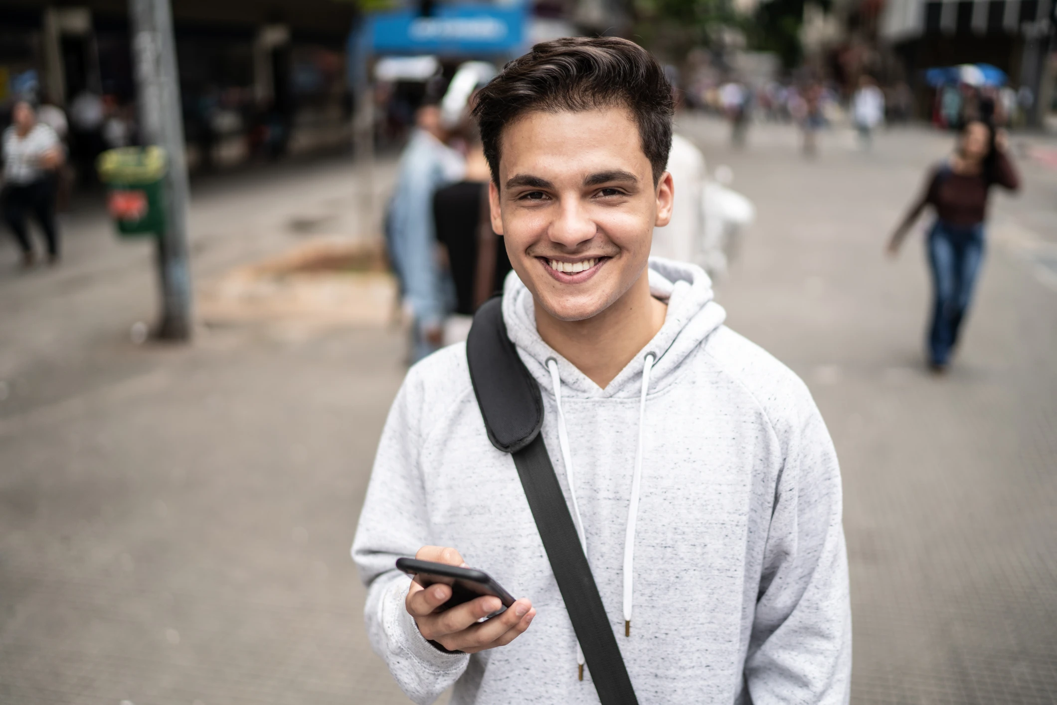 Jovem estudante sorridente caminhando pela rua segurando um smartphone