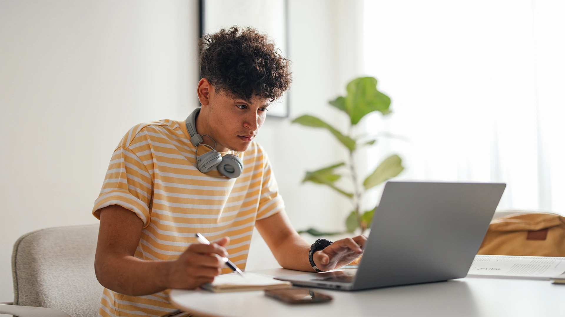 Estudante jovem concentrado usando laptop e fazendo anotações em uma mesa