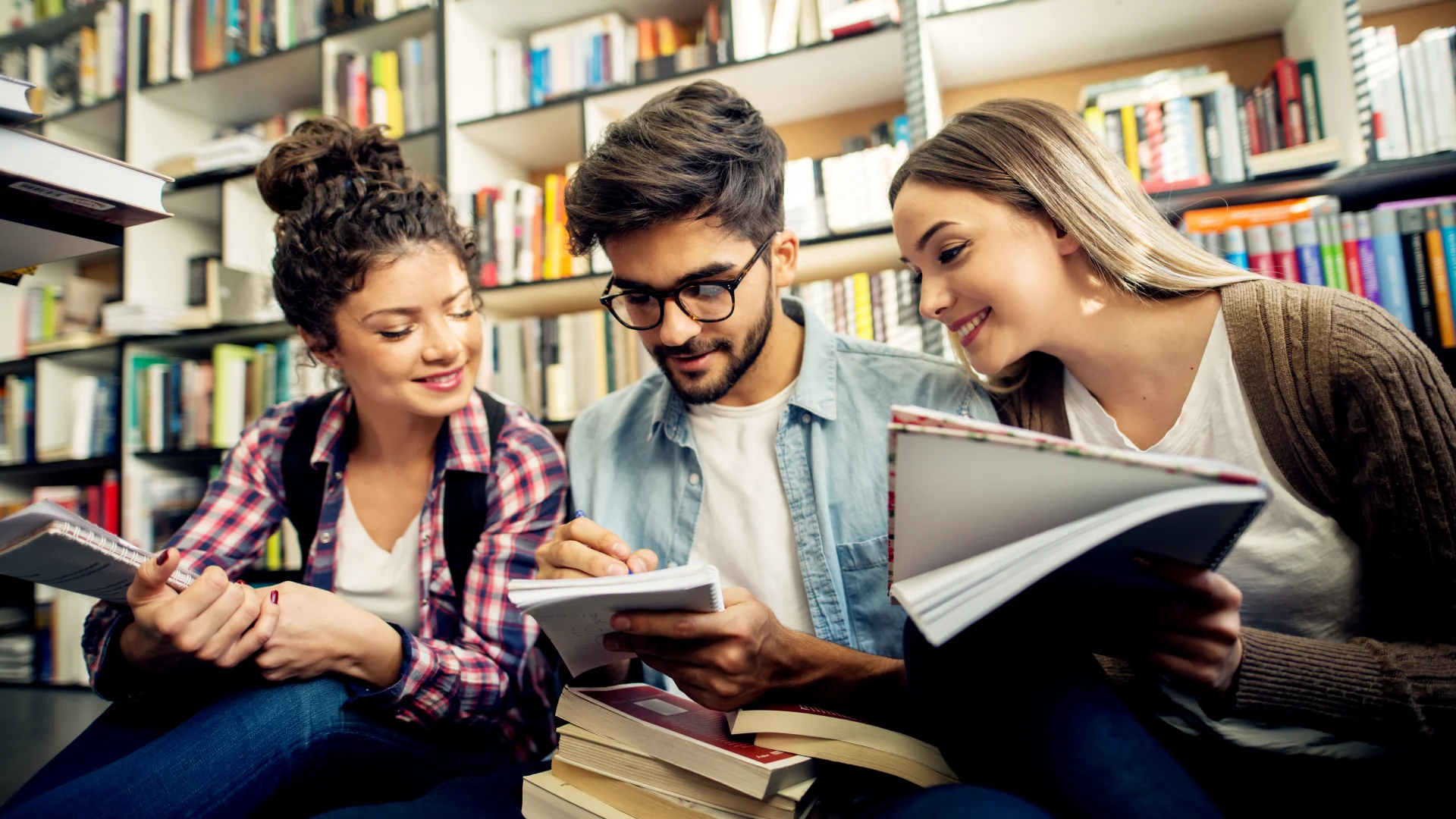 Estudantes universitários focados estudando e trocando conhecimentos em uma biblioteca acadêmica bem equipada