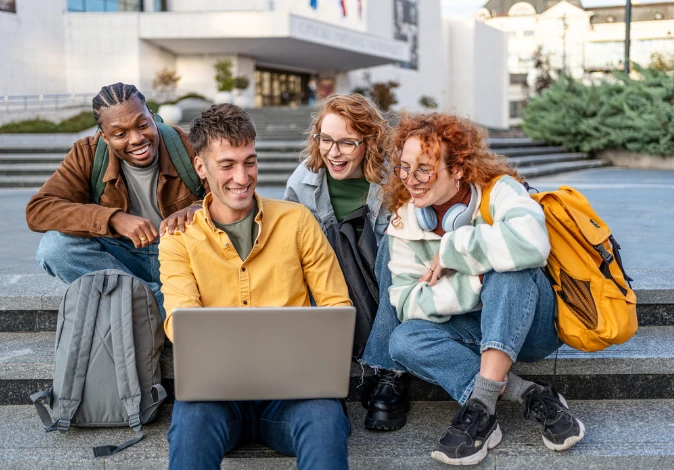 Estudantes universitários diversos colaborando em um projeto acadêmico usando um laptop ao ar livre no campus da universidade