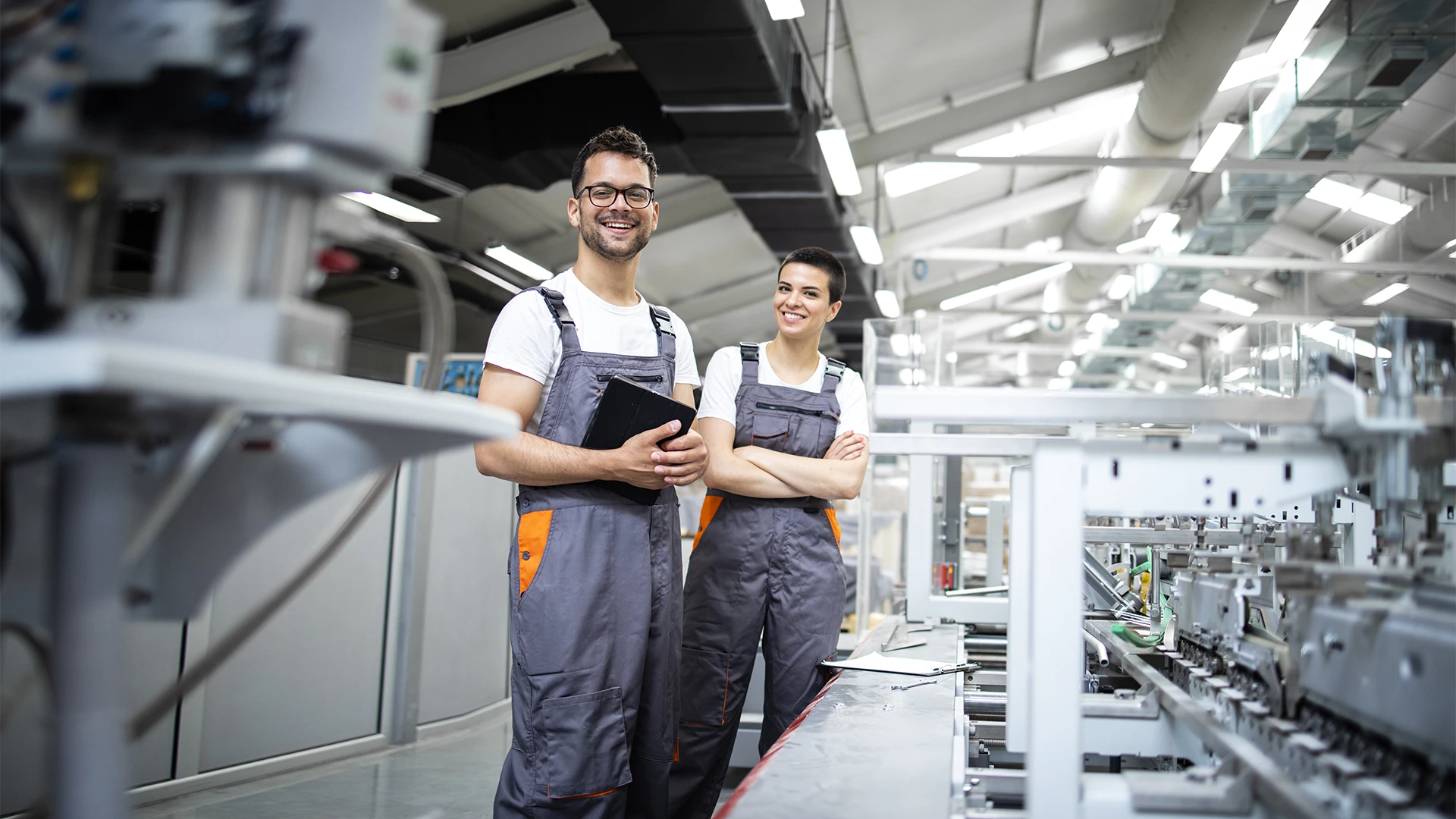 Trabalhadores sorridentes em ambiente de fábrica utilizando tablets para controle de produção