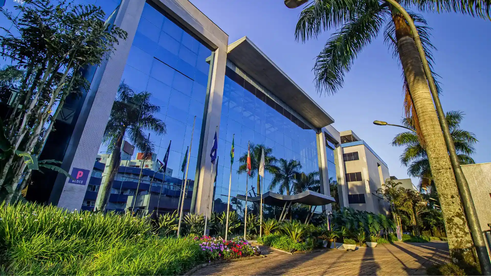 Vista externa da arquitetura moderna do campus universitário com jardins e palmeiras em um dia ensolarado