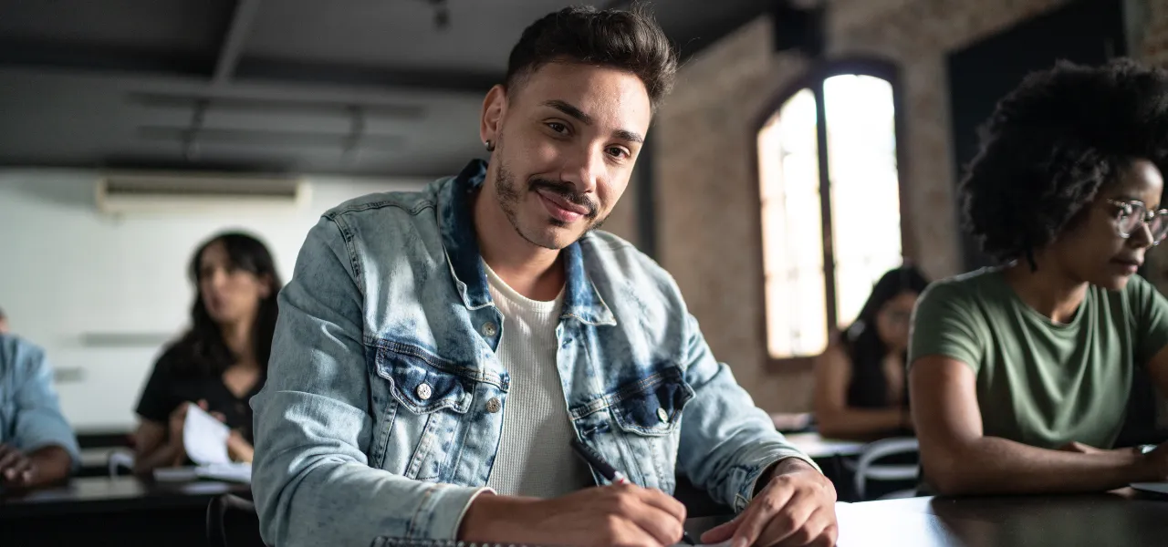 Estudante universitário sorridente escrevendo em uma sala de aula