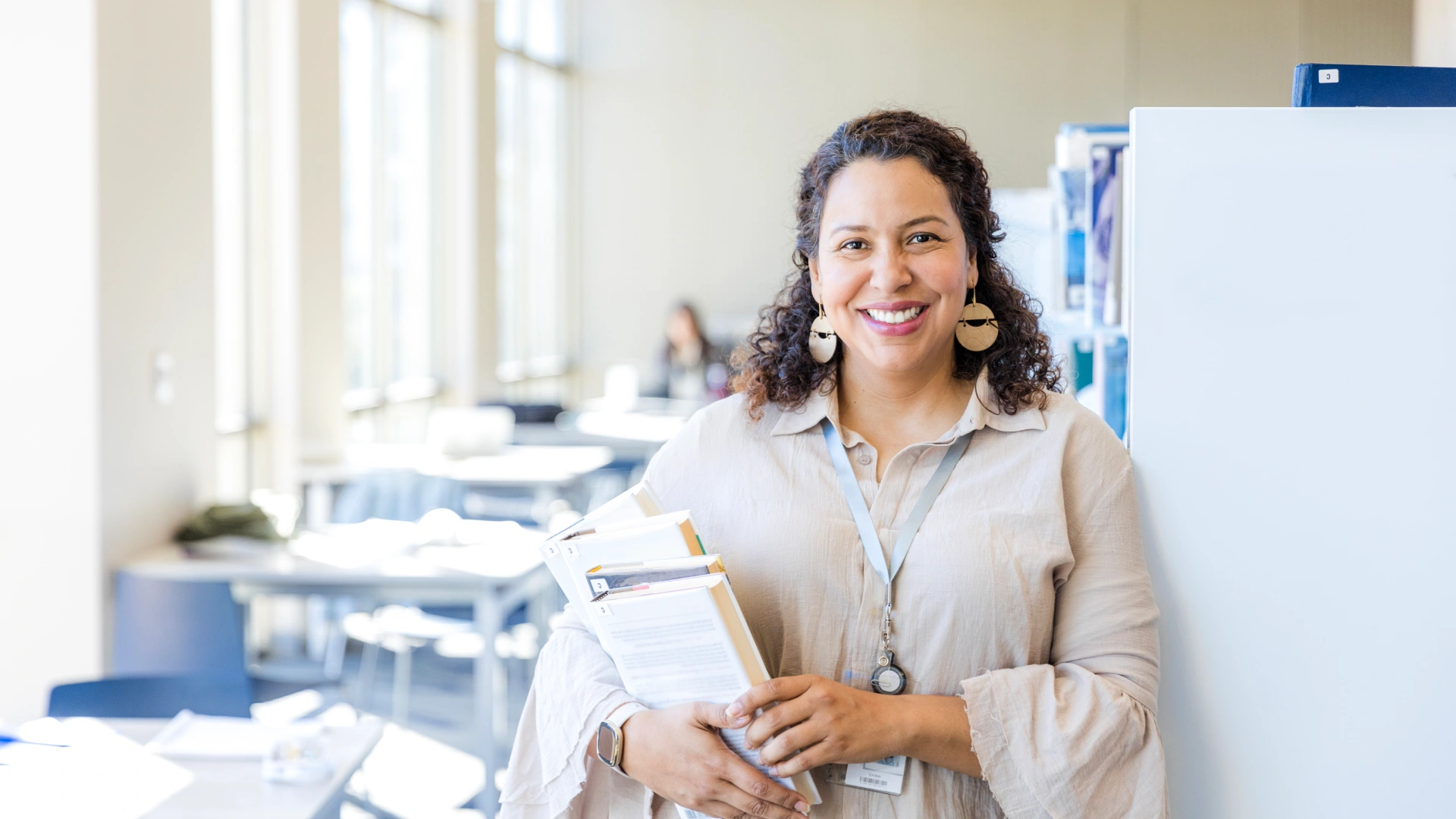 Mulher sorridente segurando livros em uma biblioteca universitária moderna