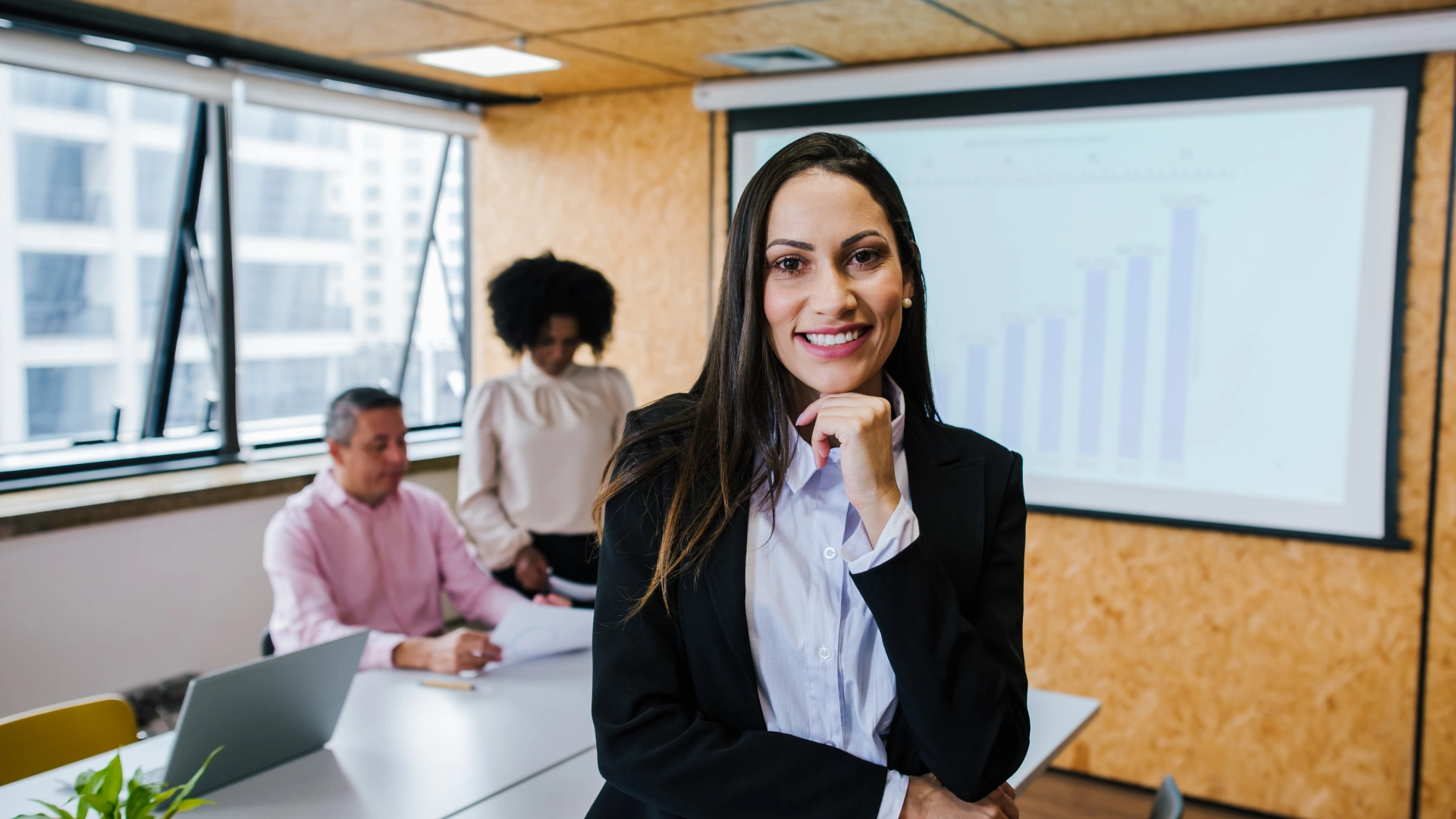 Executiva sorridente liderando reunião de negócios em um escritório corporativo moderno com equipe ao fundo