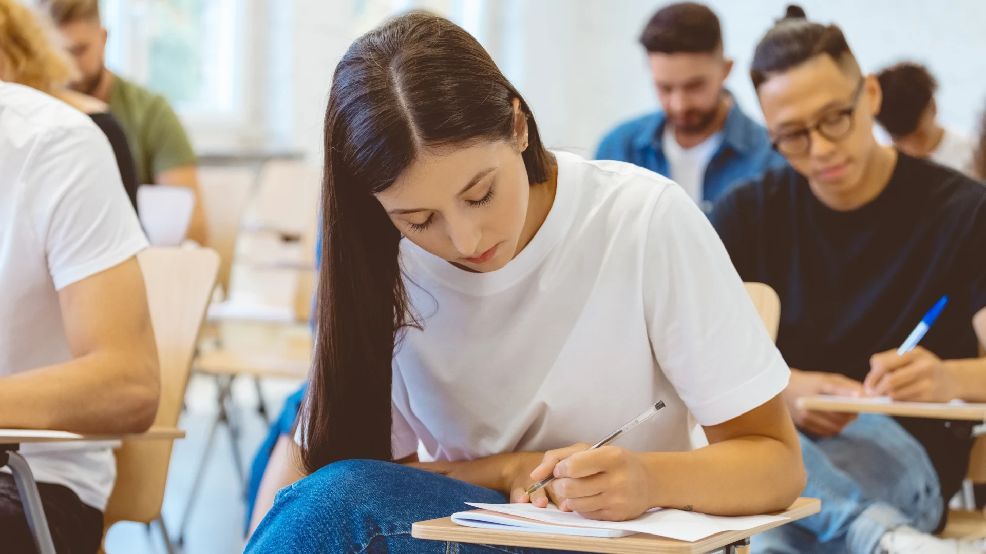 Estudante focada escrevendo em caderno durante aula em sala de aula universitária