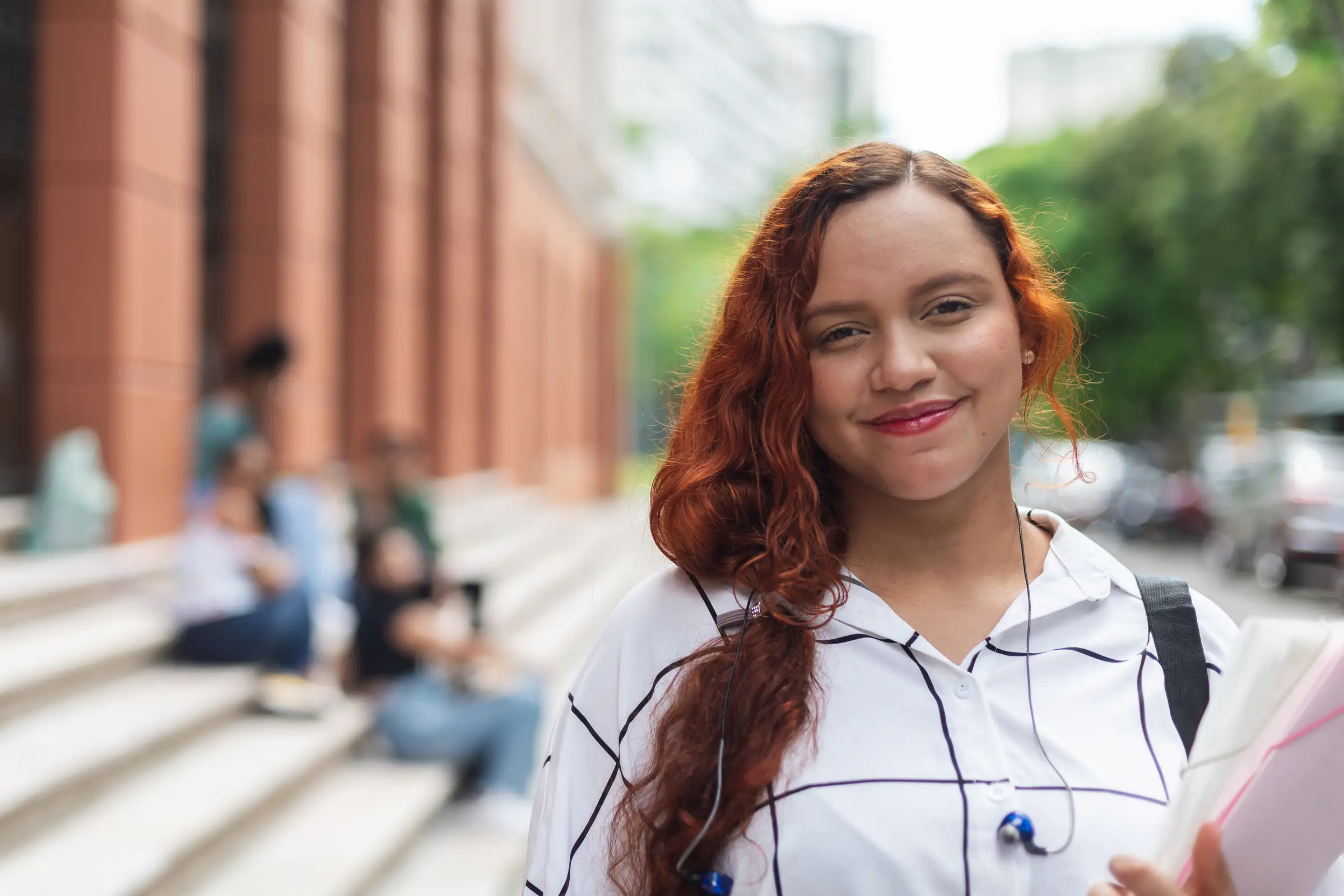 Estudante universitária ruiva sorrindo no campus com livros na mão