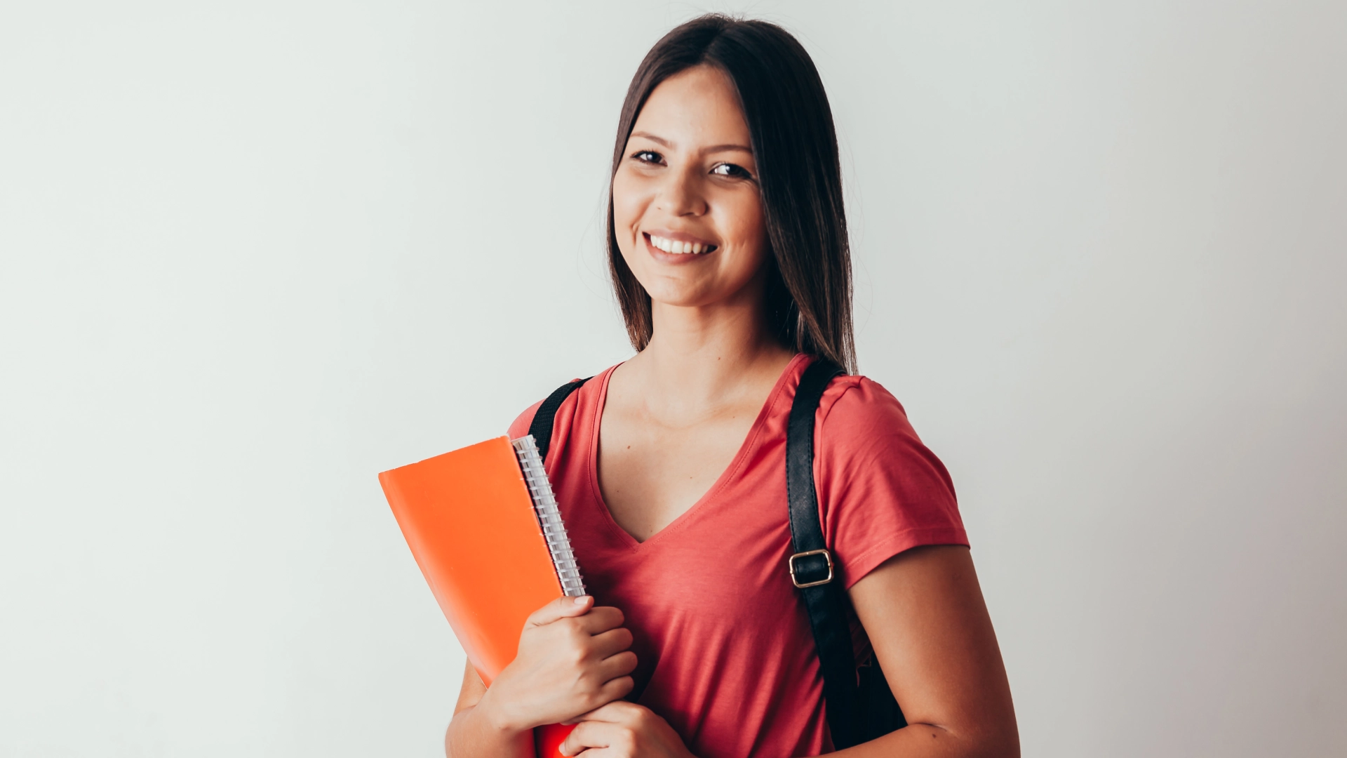Estudante universitária sorridente segurando um caderno laranja e mochila
