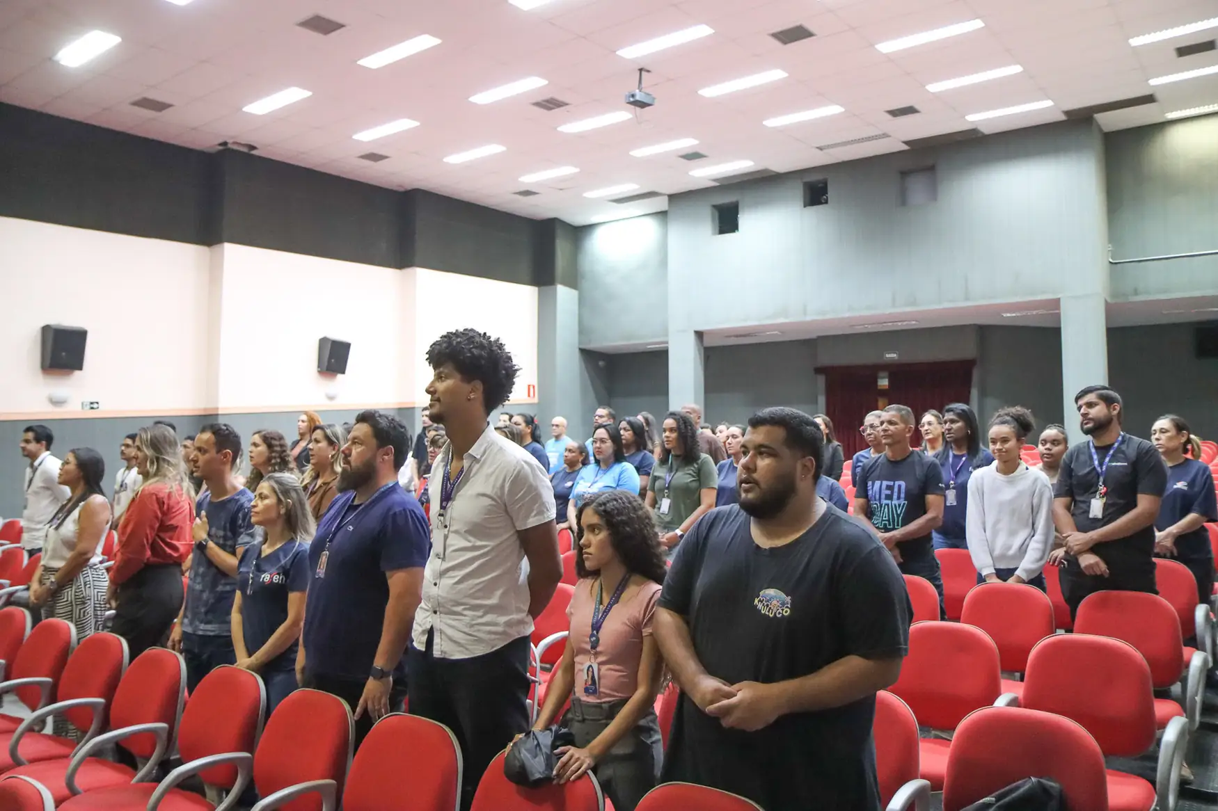 Grupo de pessoas em pé em um auditório durante um evento acadêmico ou corporativo