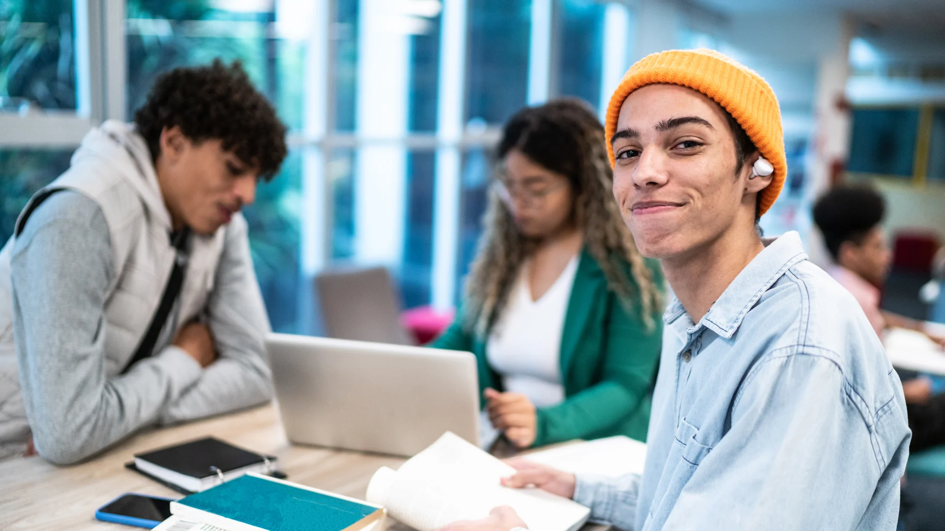 Estudantes universitários jovens realizando trabalho em grupo com notebooks e livros em uma biblioteca acadêmica