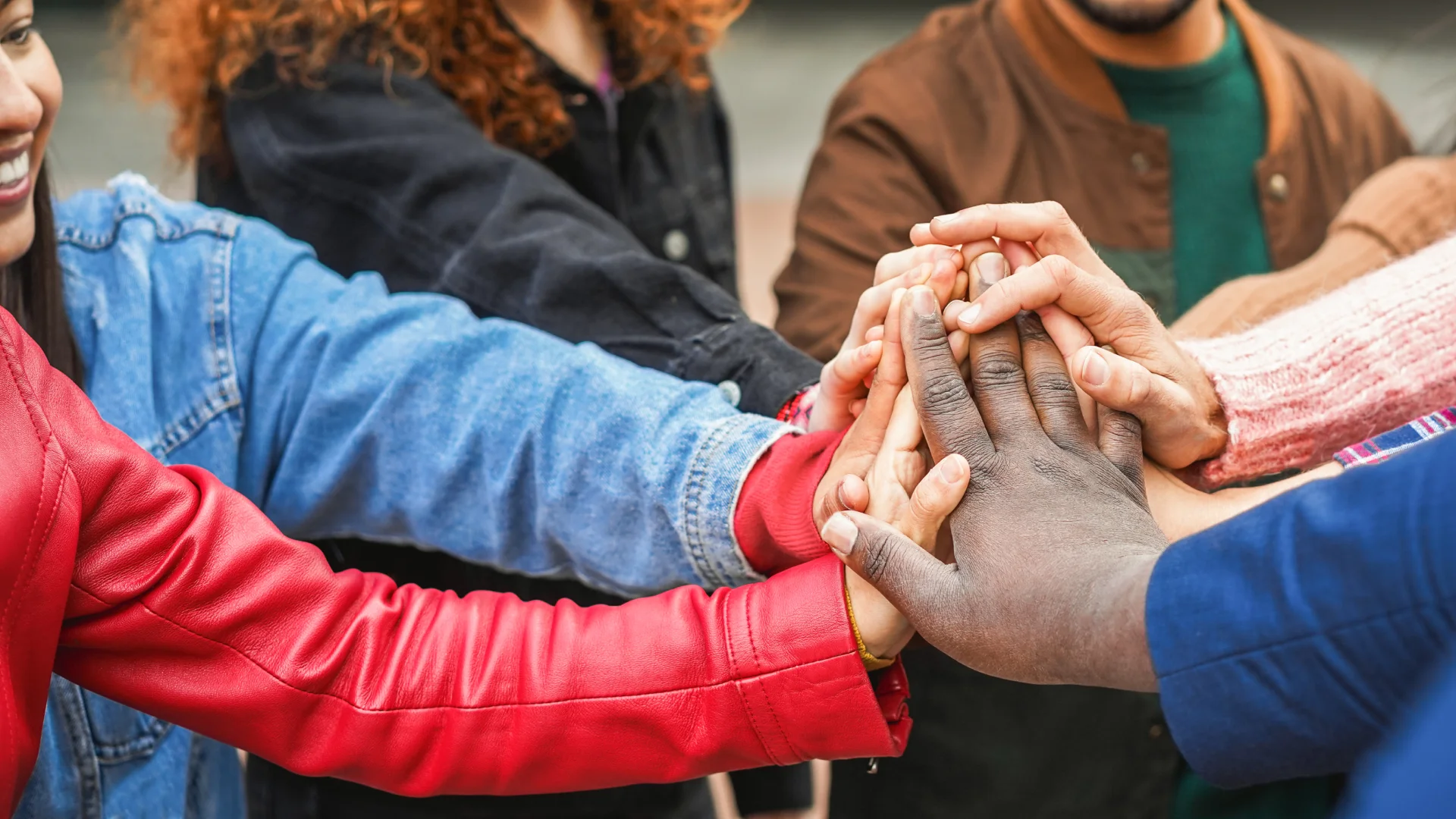 Pessoas diversas colocando as mãos juntas para representar colaboração, diversidade e união em um ambiente educacional ou profissional
