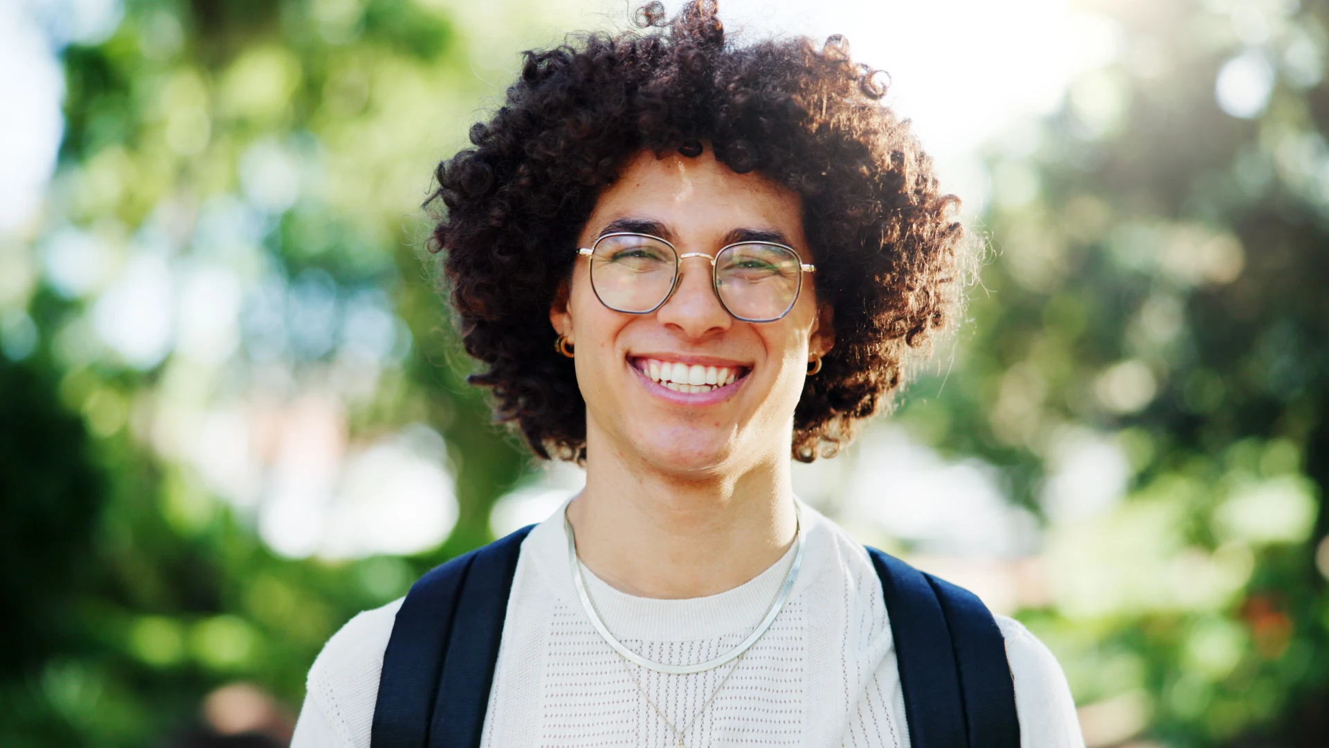 Jovem estudante universitário sorridente com cabelo cacheado e óculos em um campus universitário
