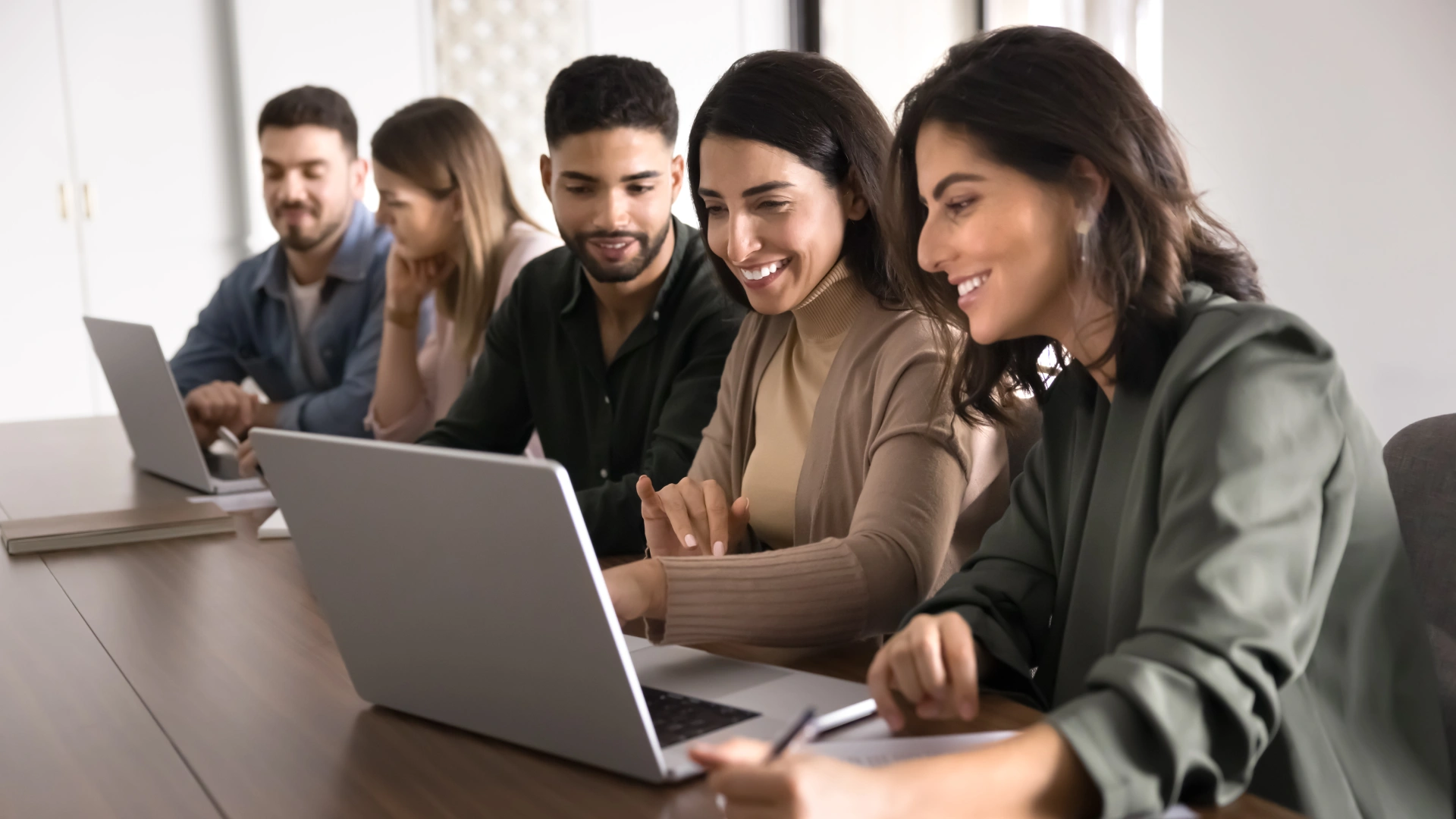 Equipe de jovens profissionais trabalhando colaborativamente em laptops em uma mesa de escritório