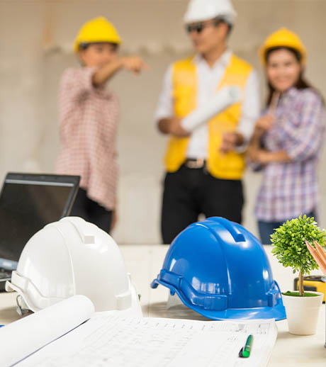 Capacetes de segurança e plantas de engenharia sobre uma mesa com equipe ao fundo
