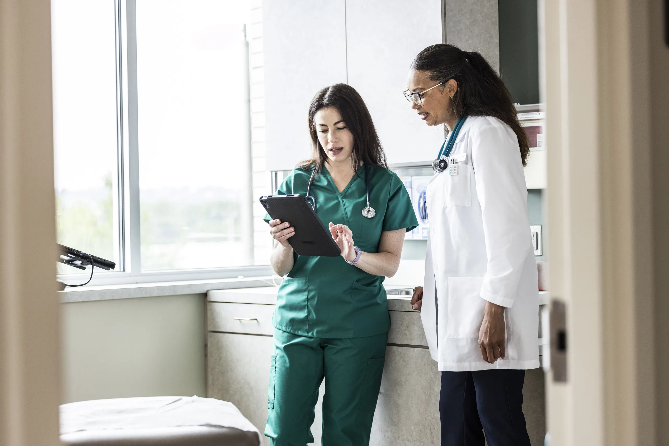 Médica e enfermeira analisando prontuário digital em tablet no hospital