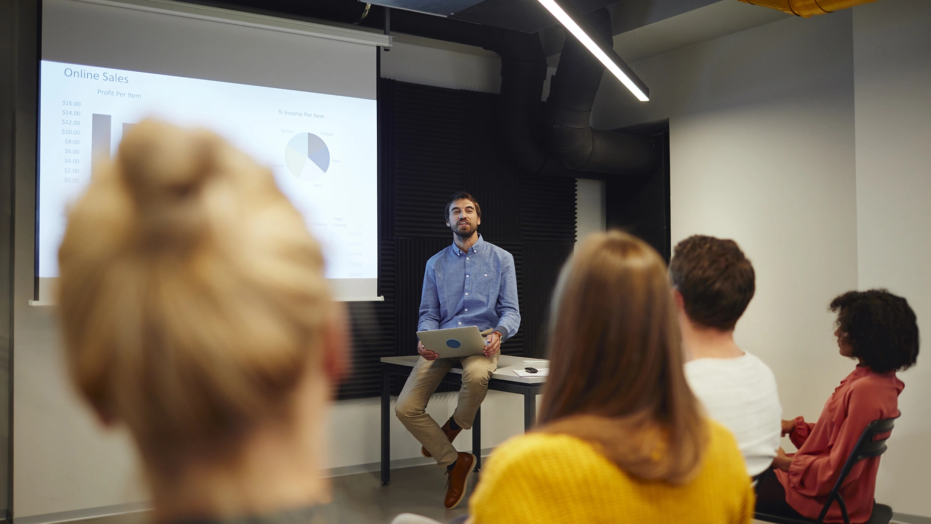 Homem apresentando dados de vendas online para uma equipe em uma sala de reuniões corporativa