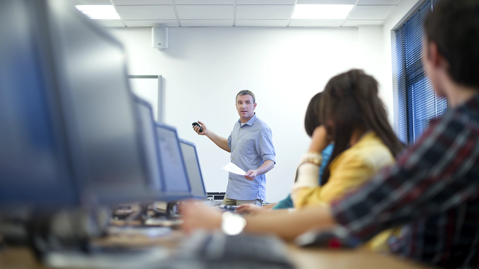 Professor ministrando aula em laboratório de informática para alunos