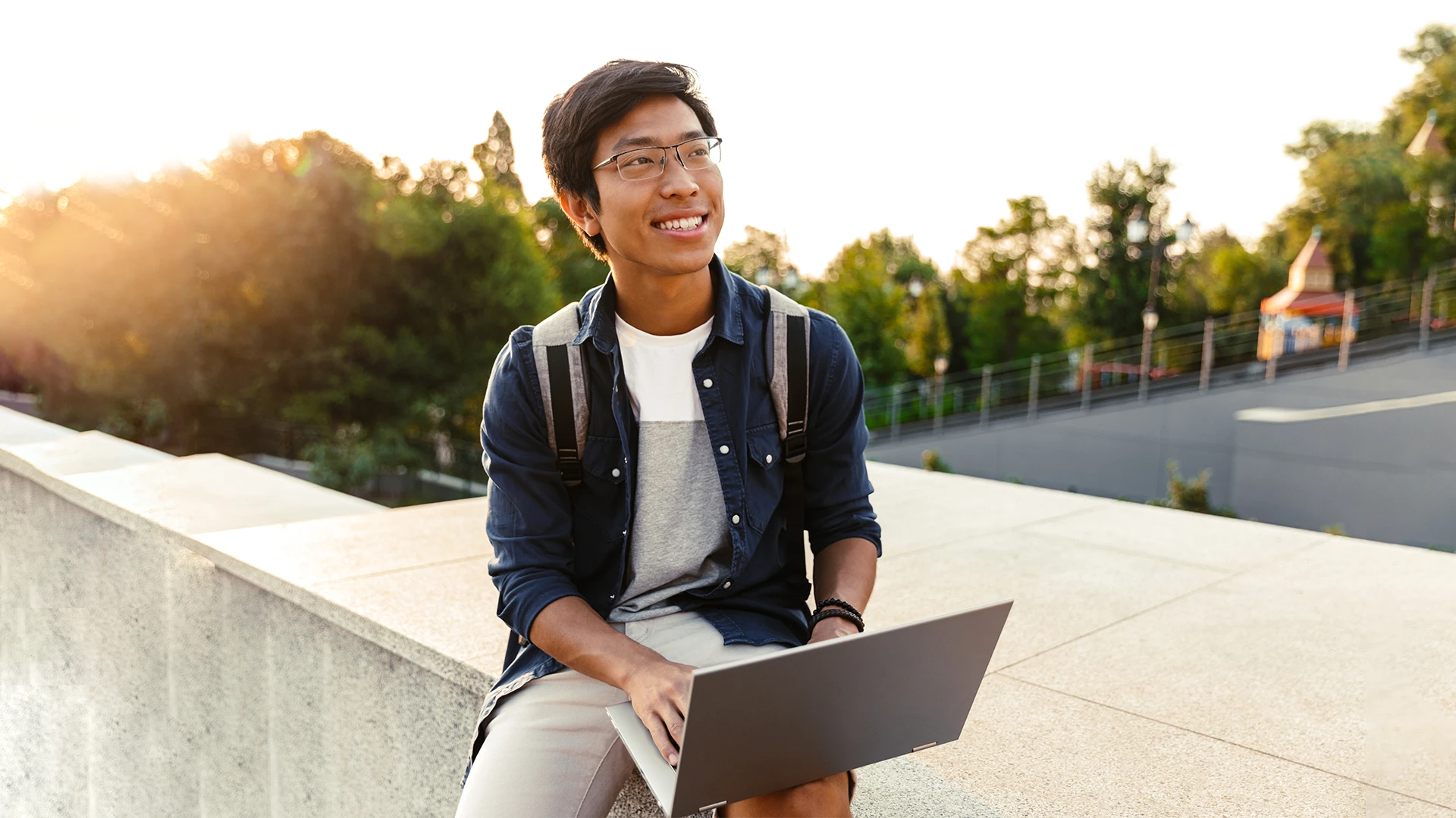 Estudante universitário sorridente usando laptop ao ar livre durante o pôr do sol