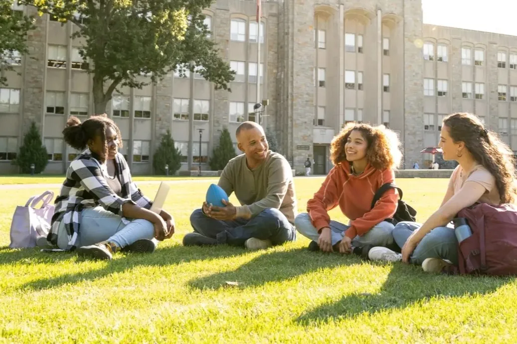 Grupo de estudantes universitários diversos sentados na grama do campus