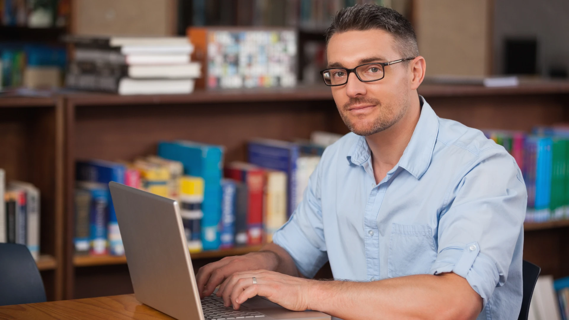 Professor universitário ou estudante utilizando notebook para pesquisa acadêmica na biblioteca da faculdade