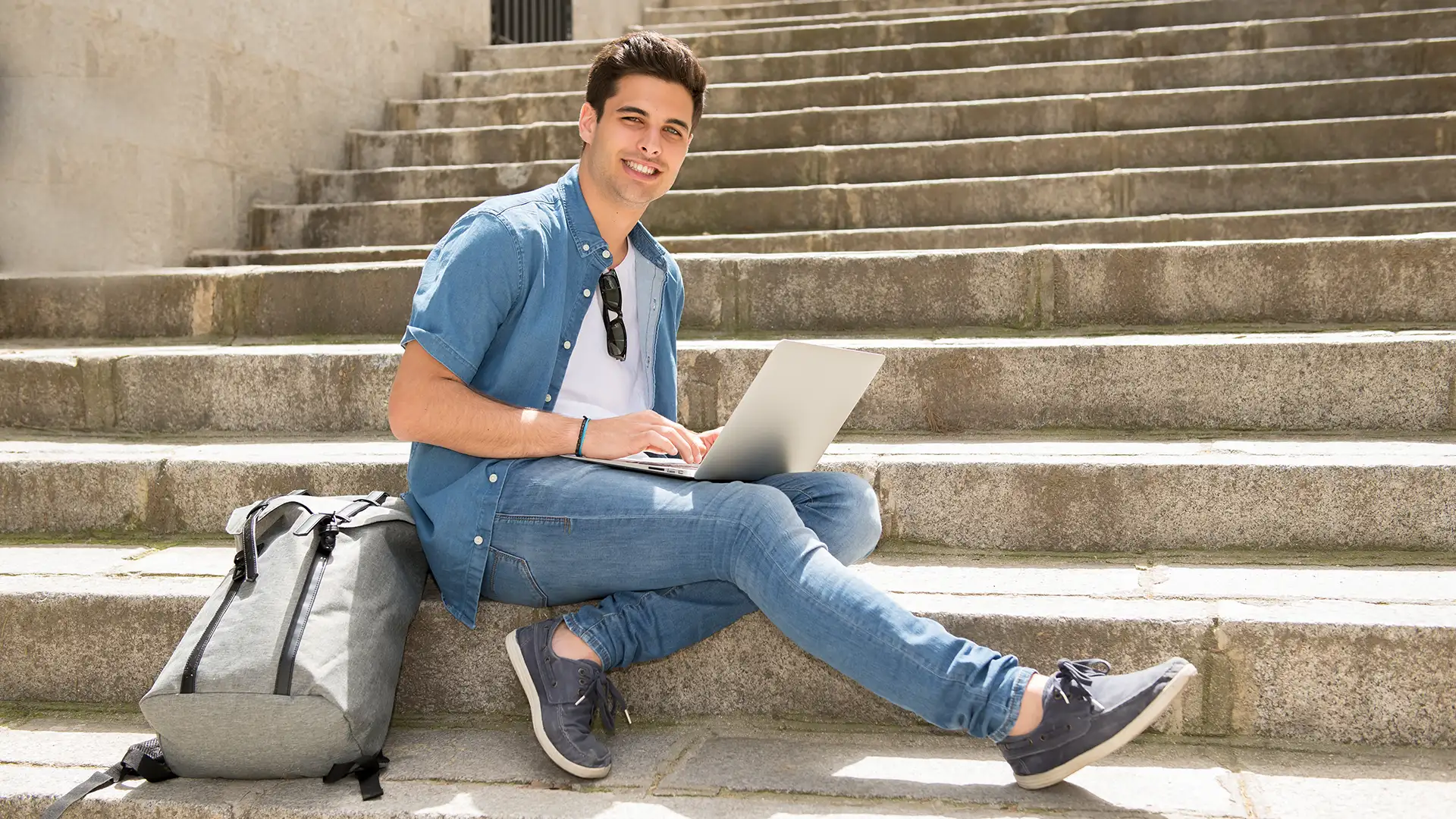 Estudante universitário sentado em escadaria usando laptop