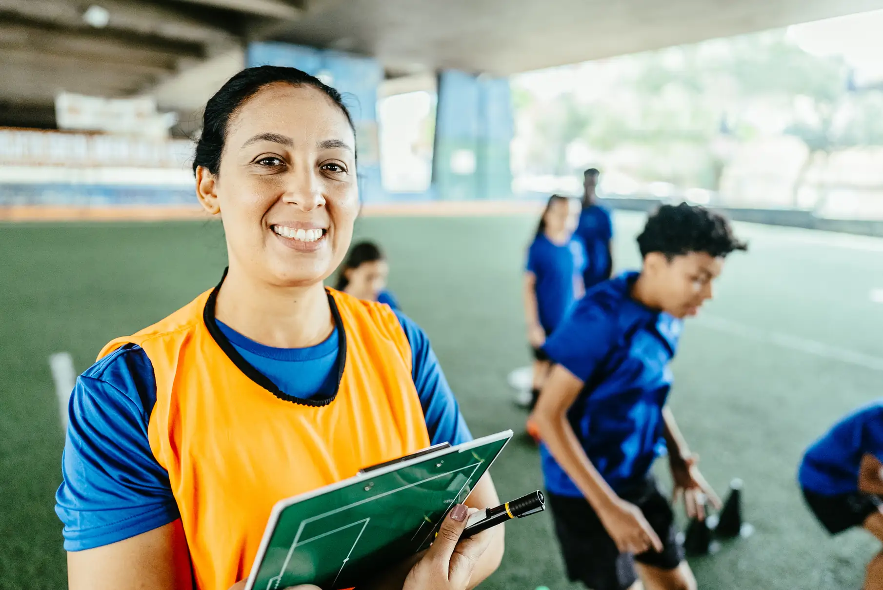 Treinadora de futebol sorridente segurando uma prancheta tática em uma quadra esportiva