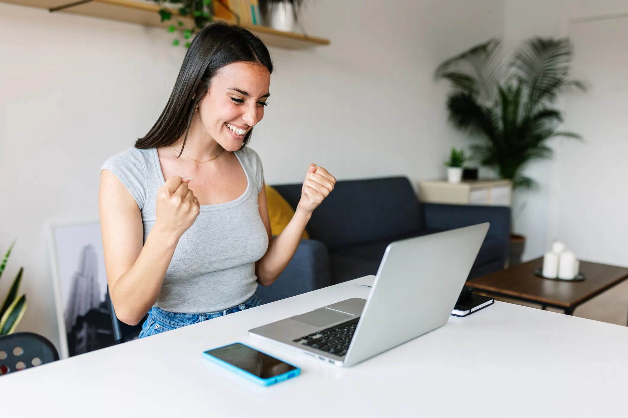 Mulher jovem celebrando sucesso profissional ou educacional com laptop em um escritório moderno em casa para ilustrar produtividade.