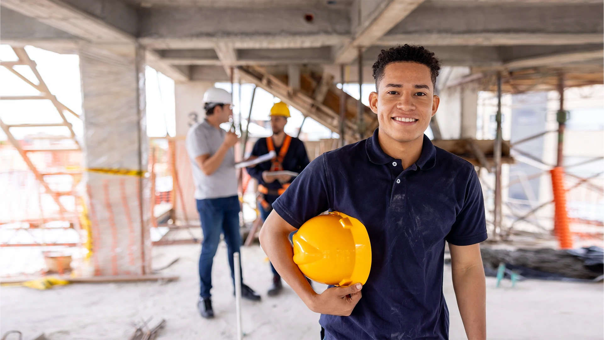 Estudante de engenharia civil sorrindo em um canteiro de obras segurando um capacete amarelo