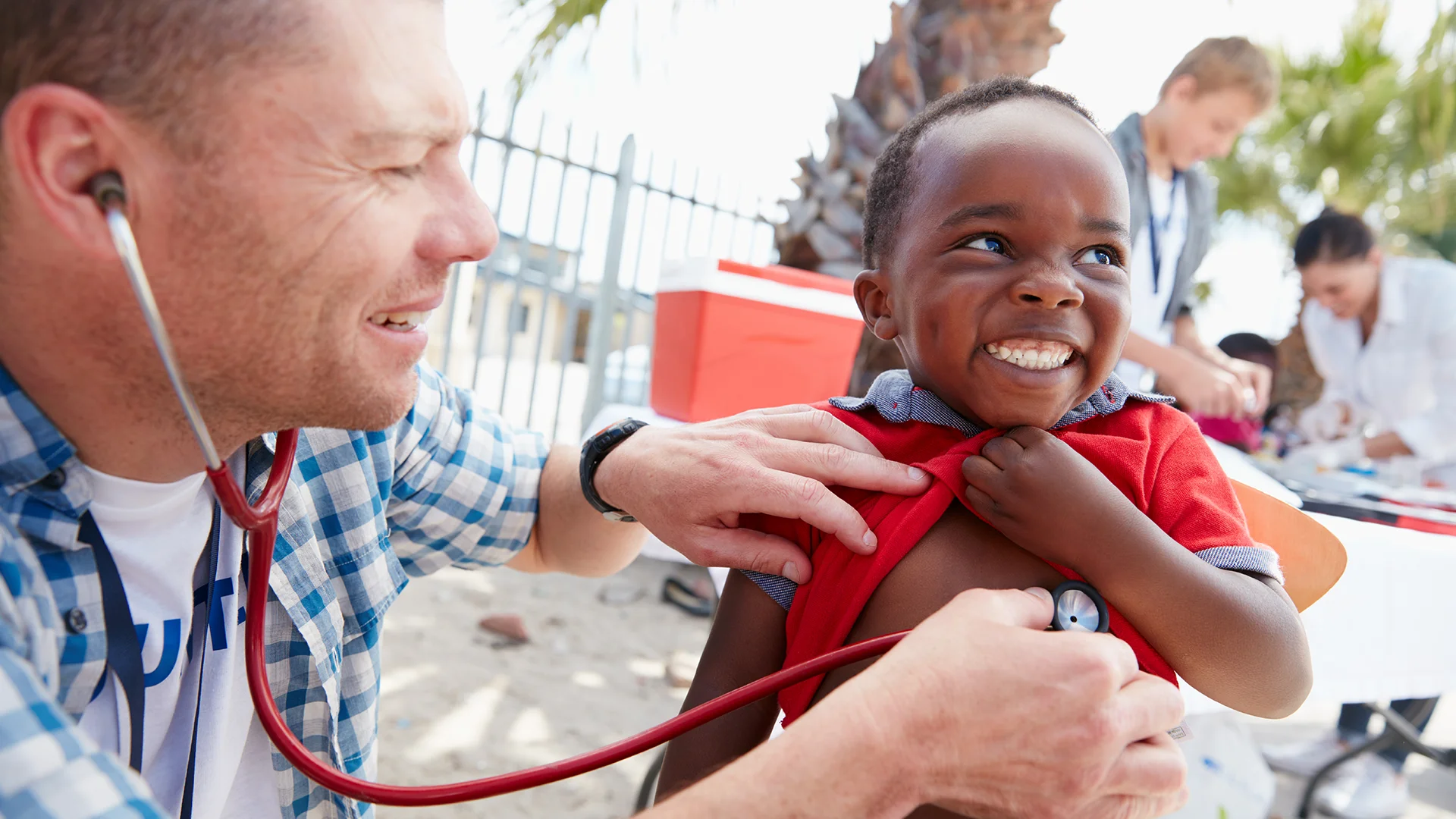 Médico voluntário realizando exame clínico com estetoscópio em uma criança sorridente durante ação social