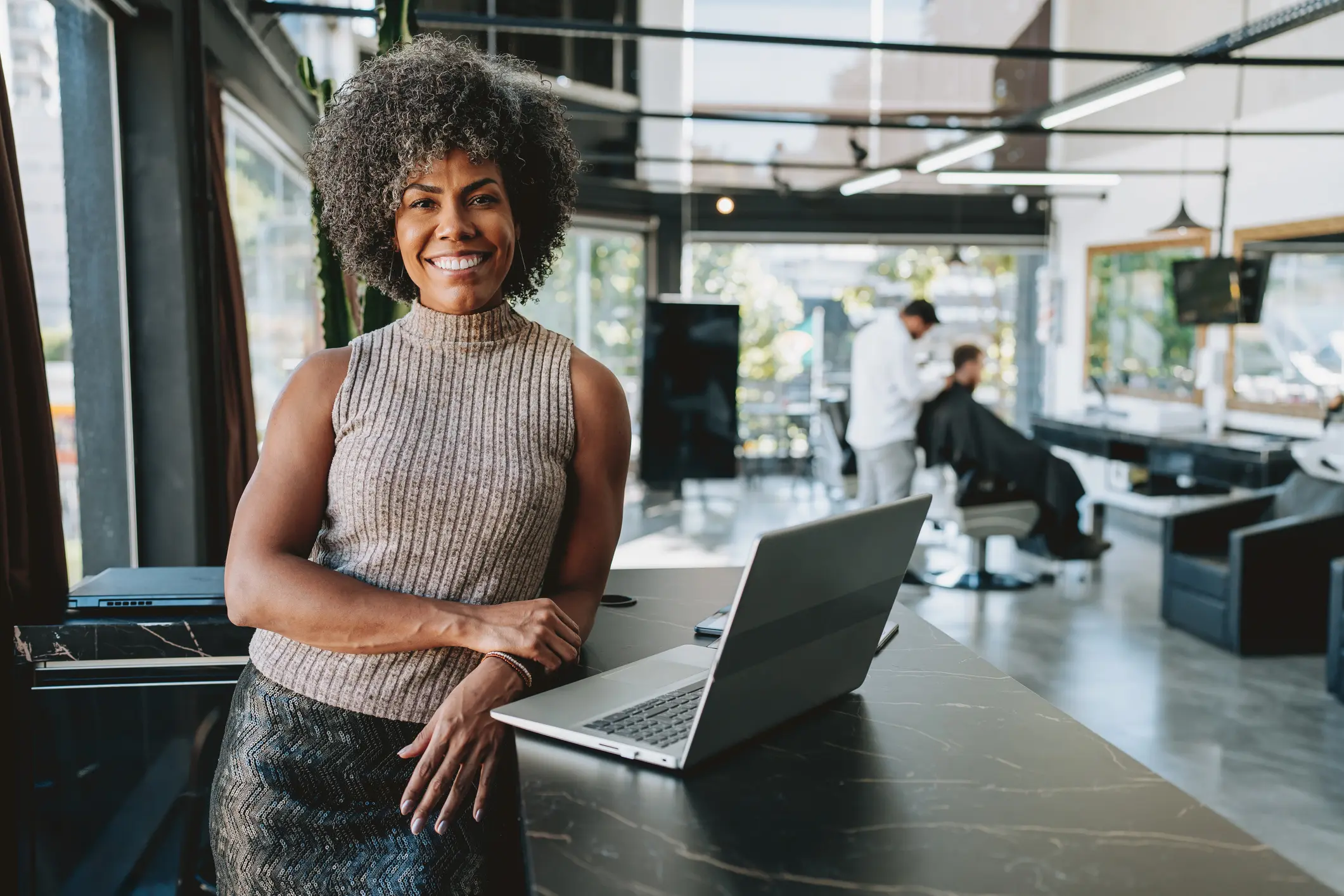 Empreendedora sorridente em seu salão de beleza moderno usando um laptop