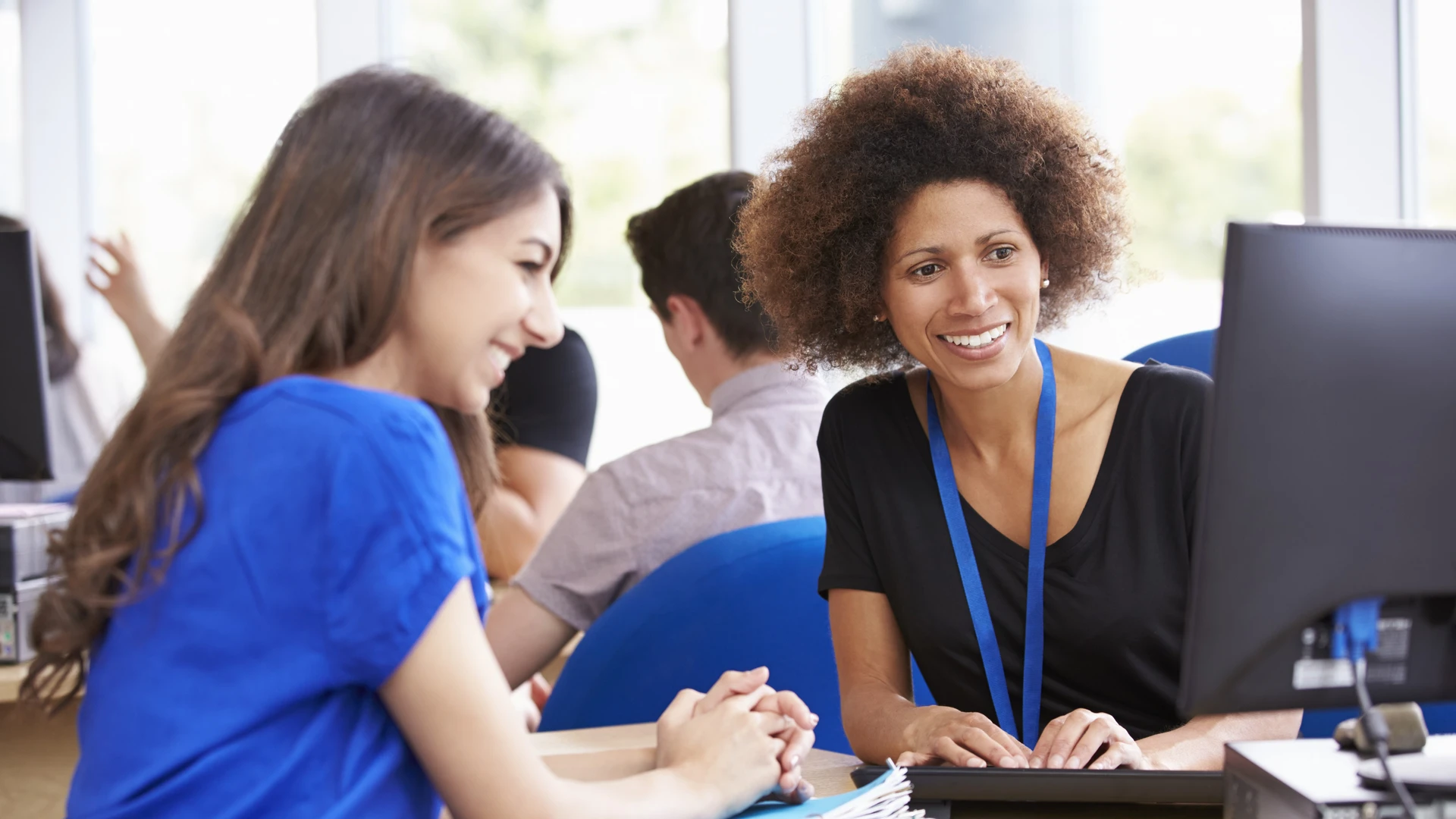 Professora orientando estudante em computador durante aula prática no laboratório da universidade