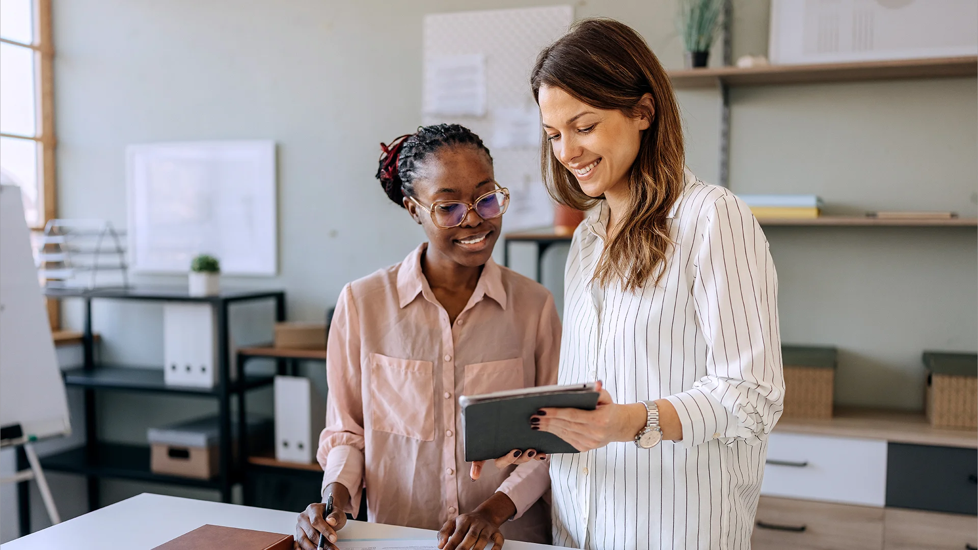 Duas mulheres colaborando em um escritório moderno usando um tablet e tomando notas