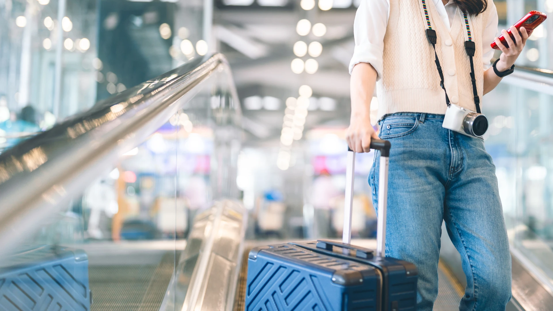 Viajante usando smartphone e carregando mala de viagem em uma escada rolante dentro de um aeroporto moderno