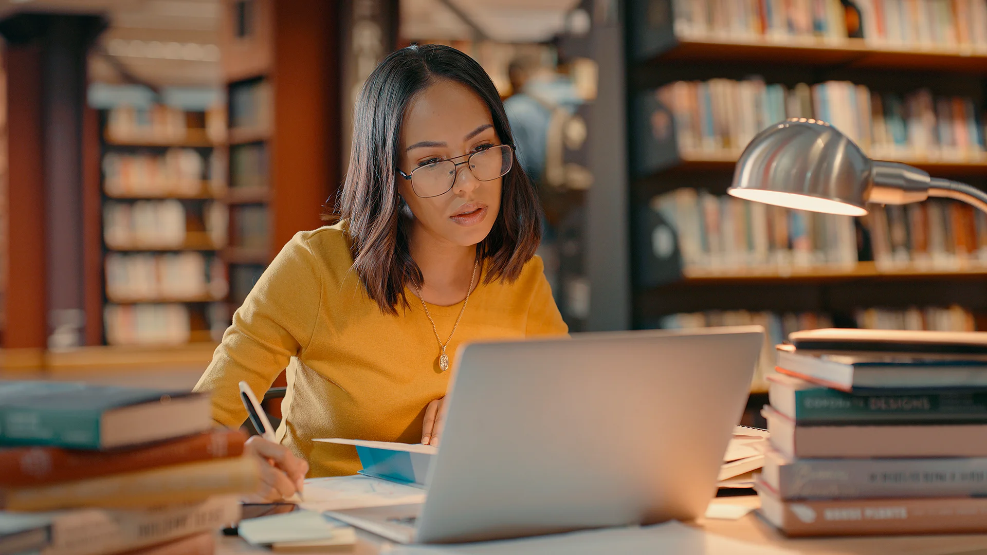 Estudante focada usando notebook e fazendo anotações em uma biblioteca