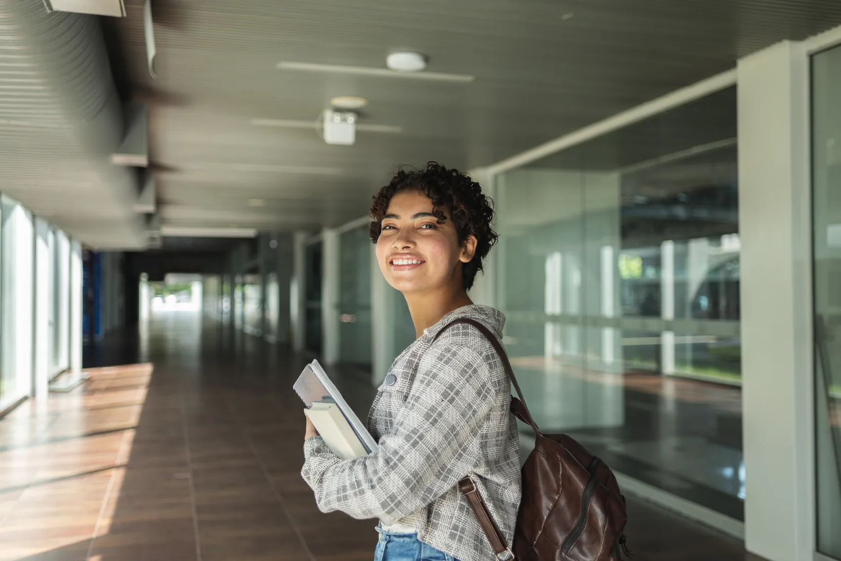 Estudante universitária feliz segurando cadernos em um campus moderno, representando o sucesso e a dedicação aos estudos