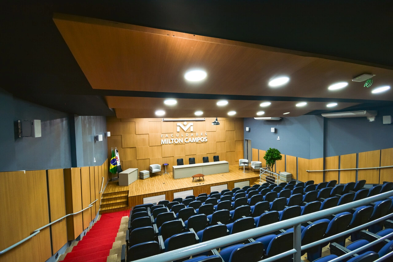 Auditório das Faculdades Milton Campos com palco, mesa e poltronas dispostas em estilo anfiteatro