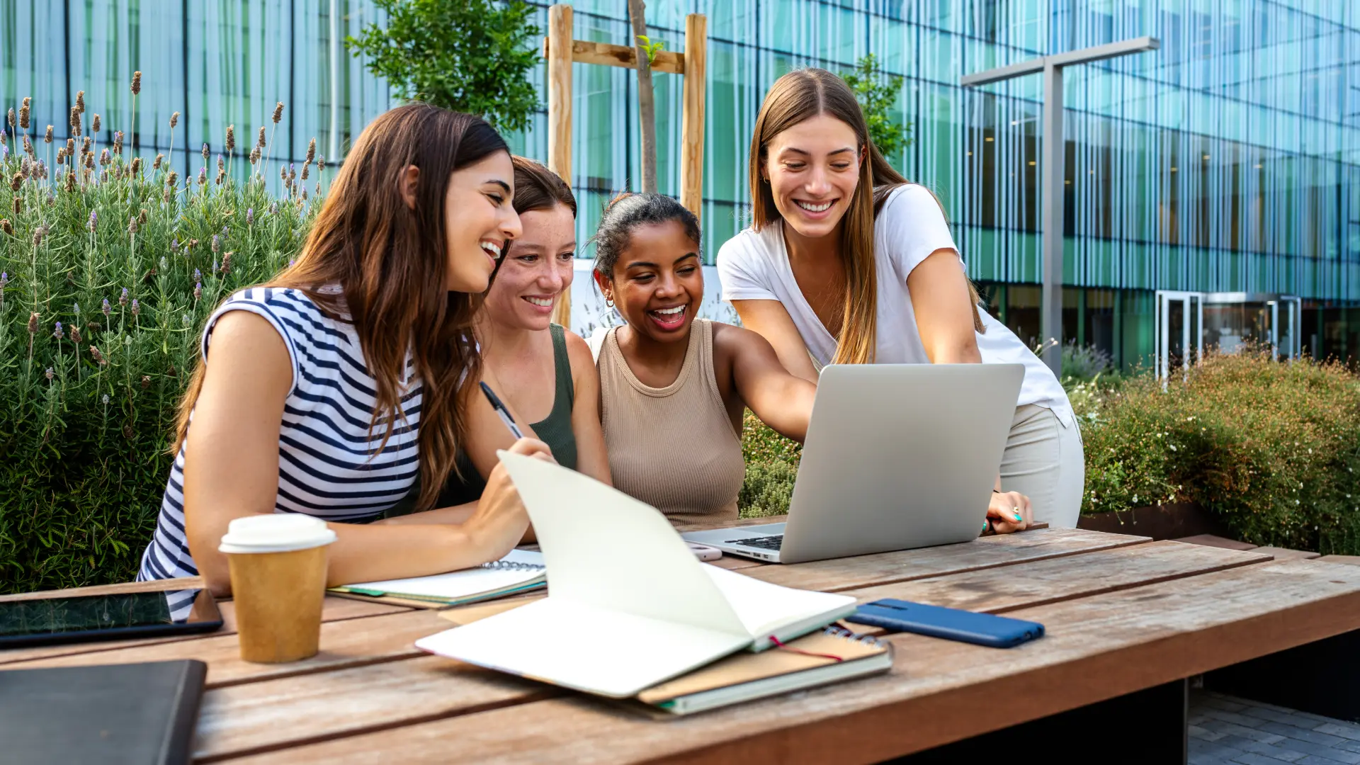 Estudantes universitárias colaborando em um projeto acadêmico usando um laptop em um ambiente de estudo moderno ao ar livre