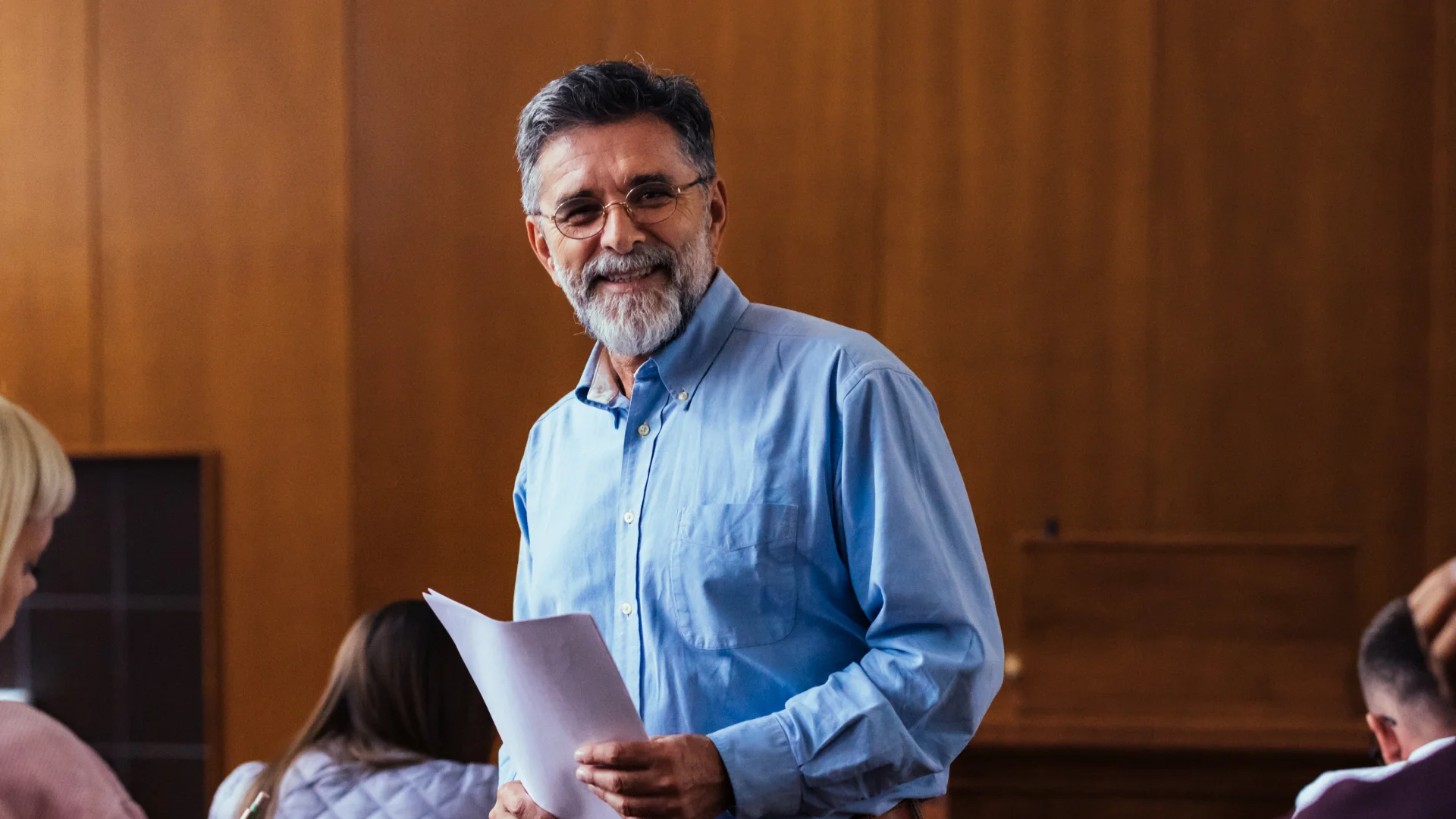 Professor experiente conduzindo aula em ambiente acadêmico com alunos ao fundo