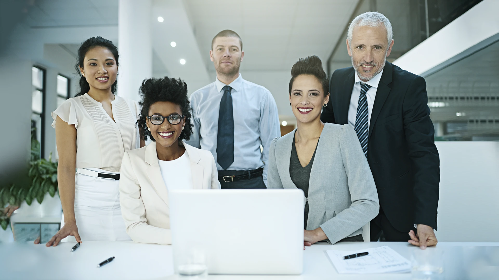 Equipe corporativa diversificada posando em escritório moderno com notebook
