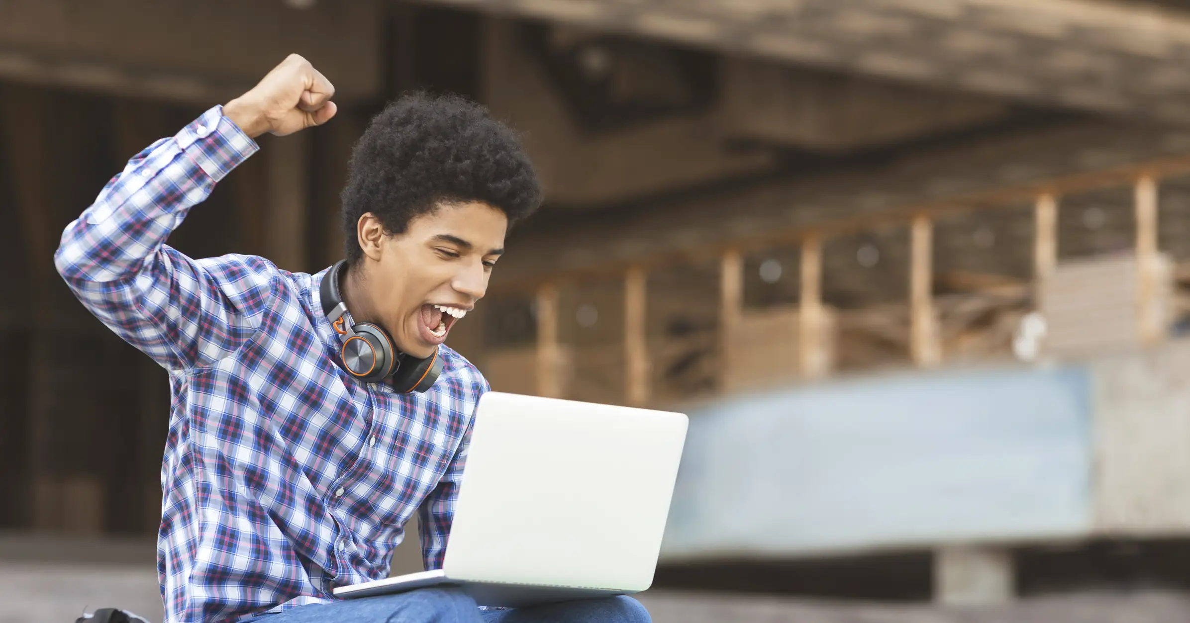Estudante universitário comemorando uma conquista acadêmica ou profissional usando seu notebook Jovem estudante negro comemorando sucesso no notebook