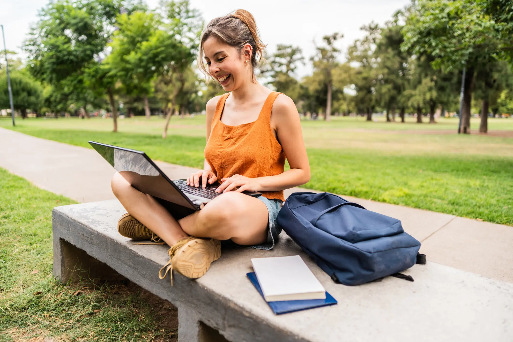 Estudante universitária aproveitando o ar livre para estudar com notebook em um parque ensolarado