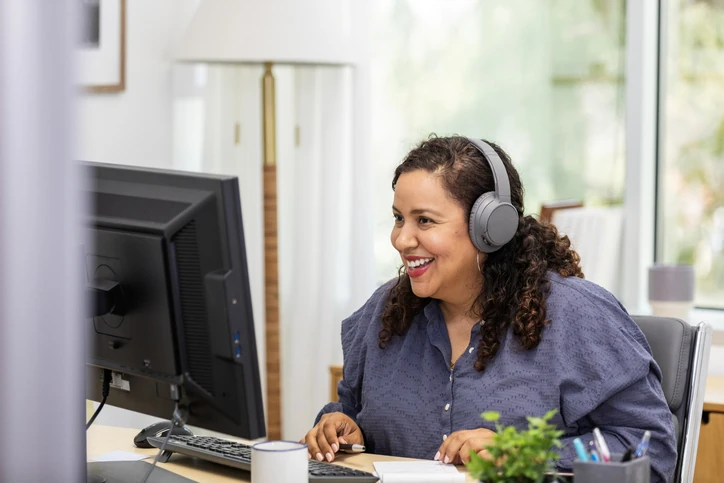Mulher sorridente trabalhando remotamente em um escritório moderno com computador e fones de ouvido para reuniões online