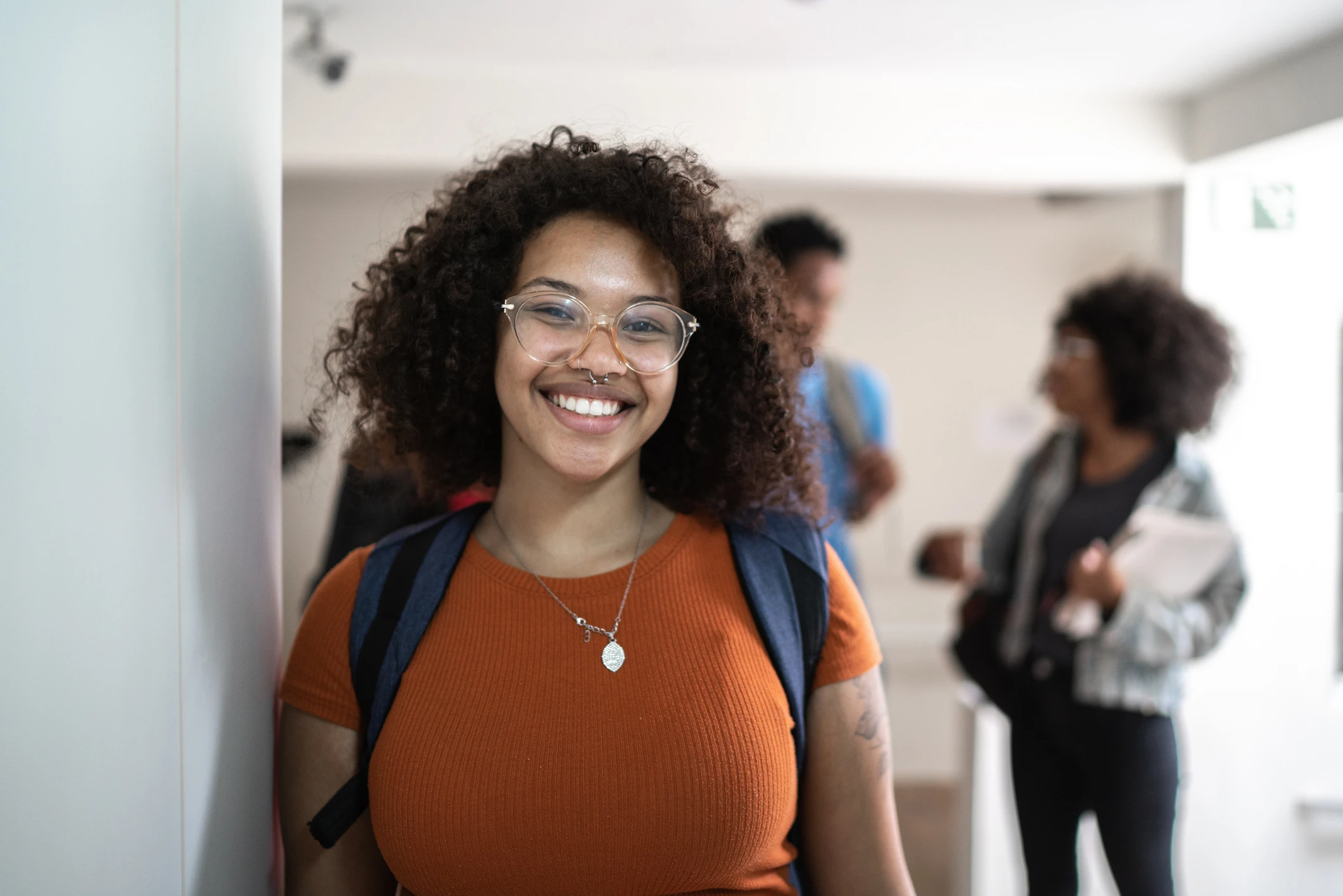 Estudante universitária negra sorrindo com mochila e óculos no campus