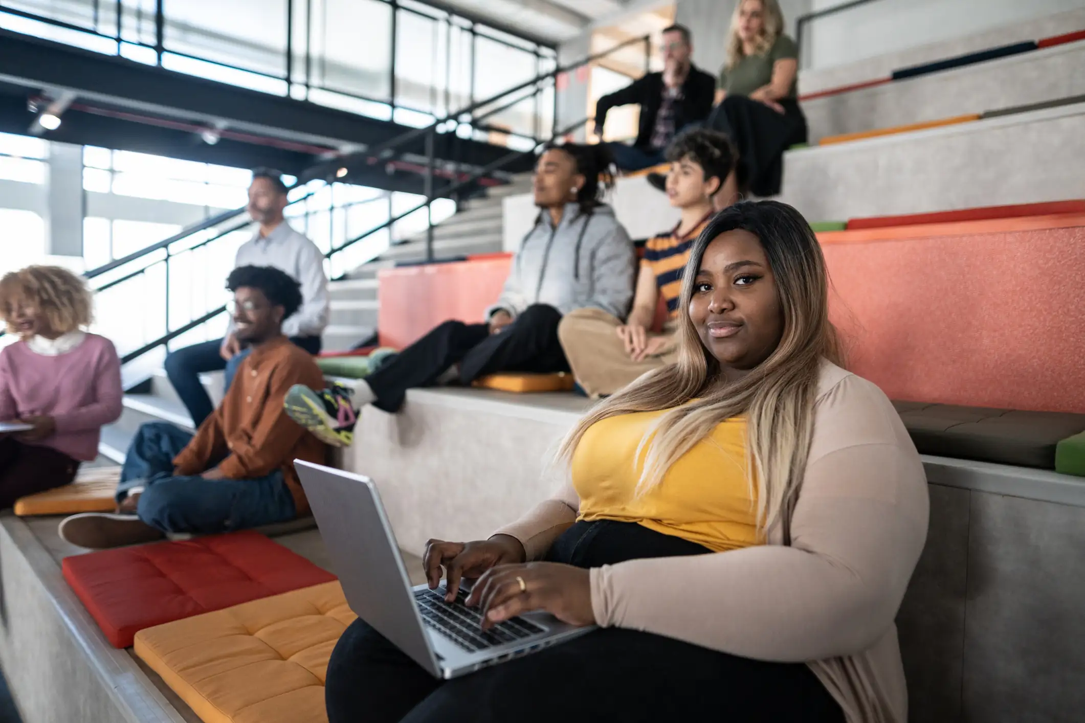 Jovem profissional ou estudante trabalhando com notebook em espaço de coworking moderno e colaborativo com equipe ao fundo