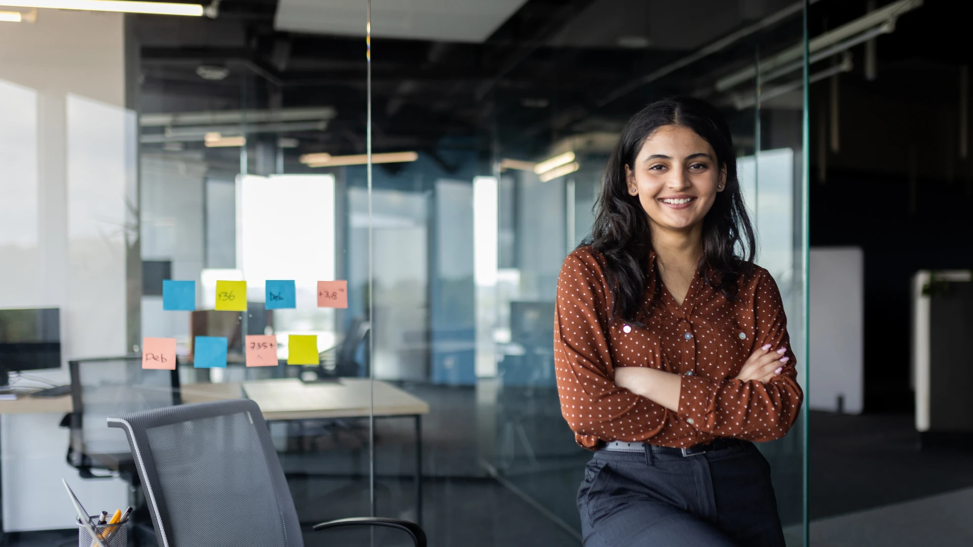 Jovem profissional sorridente em um escritório moderno com divisórias de vidro e post-its