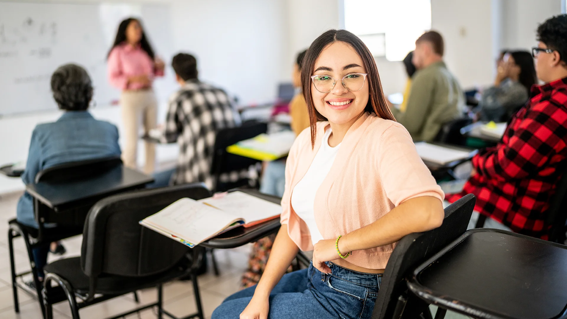 Estudante universitária sorridente sentada em sala de aula com colegas ao fundo