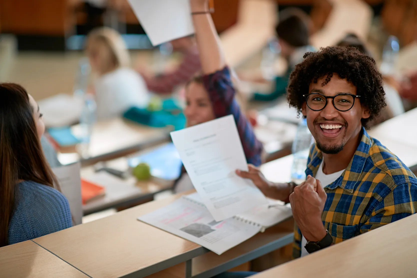 Estudante universitário feliz comemorando uma prova ou resultado acadêmico em sala de aula