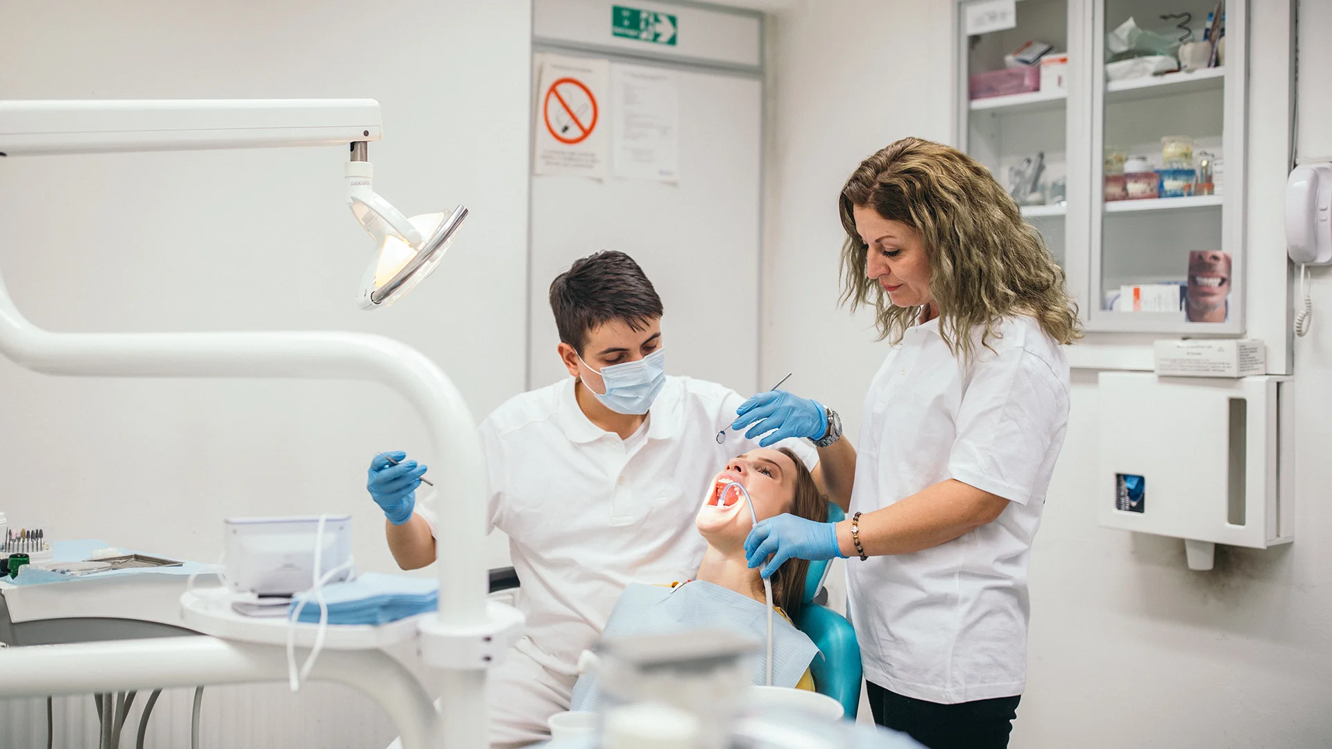 Dentista e assistente realizando procedimento odontológico em paciente no consultório